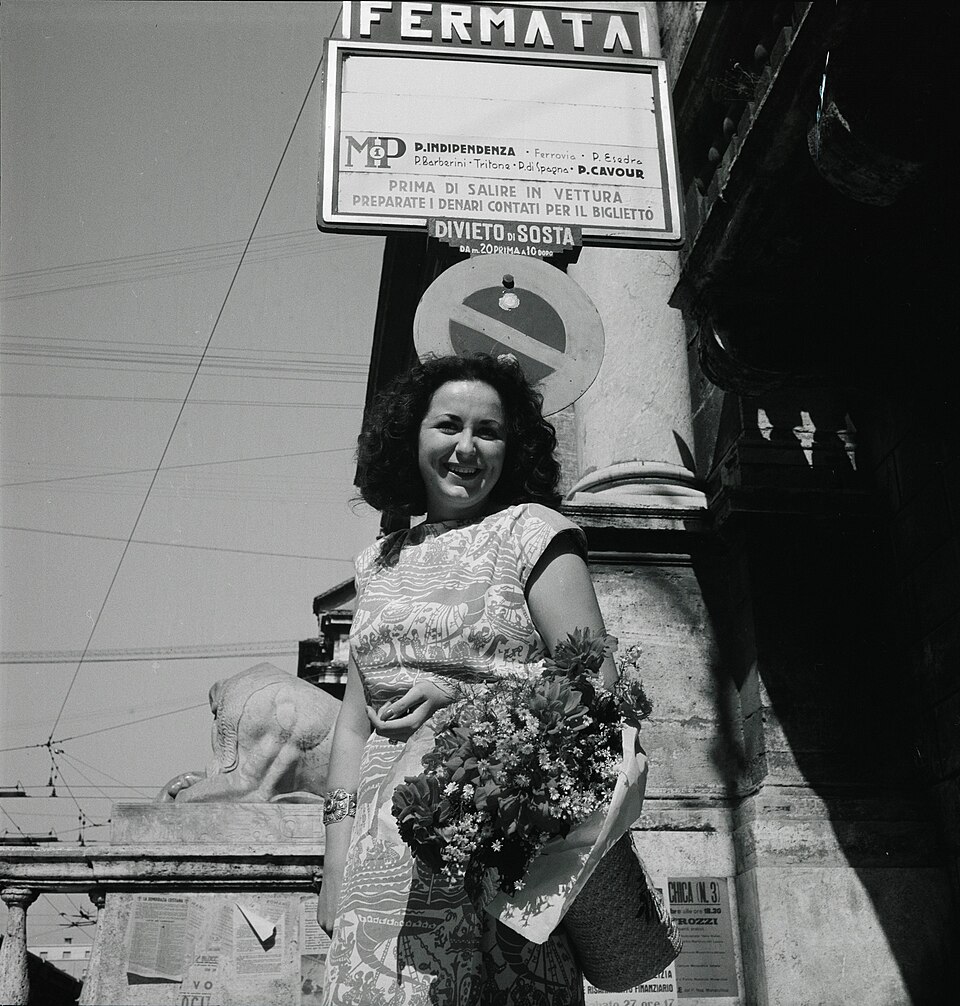 Una donna sorride con un mazzo di fiori a una fermata dell'autobus, Roma 1947